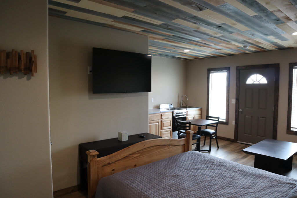 Cabin interior at Track One Lodging showing bed, kitchenette, and entry door — Railyard 26, Oshkosh, Nebraska